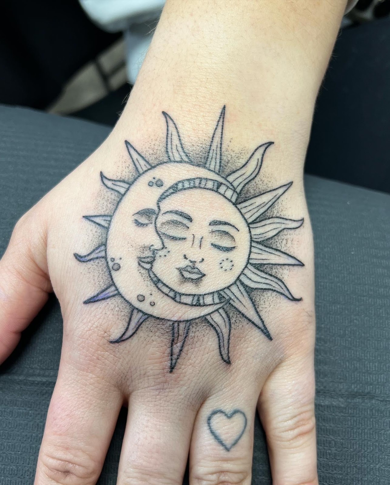 Fine line sun and crescent moon tattoo on the back of a hand