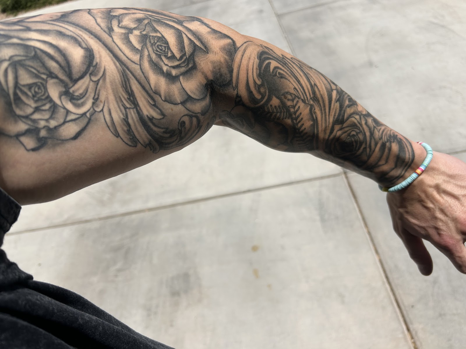 Black and gray rose sleeve tattoo from shoulder to wrist, photographed in daylight