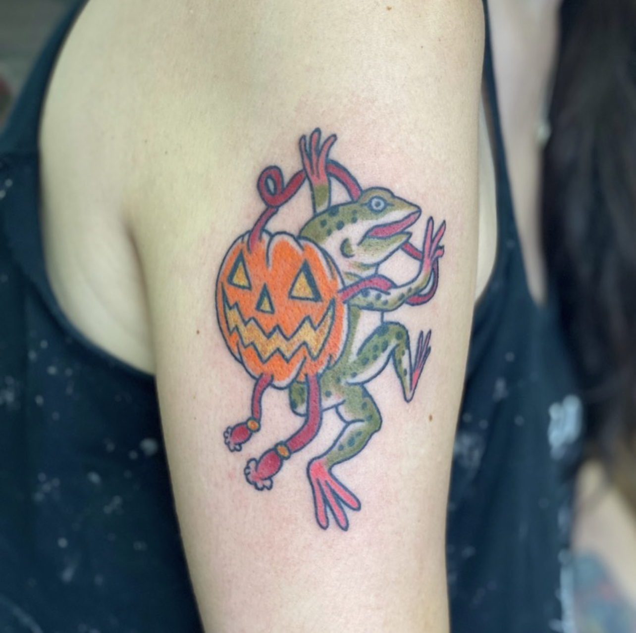 Color traditional tattoo of a frog carrying a jack o lantern on an upper arm