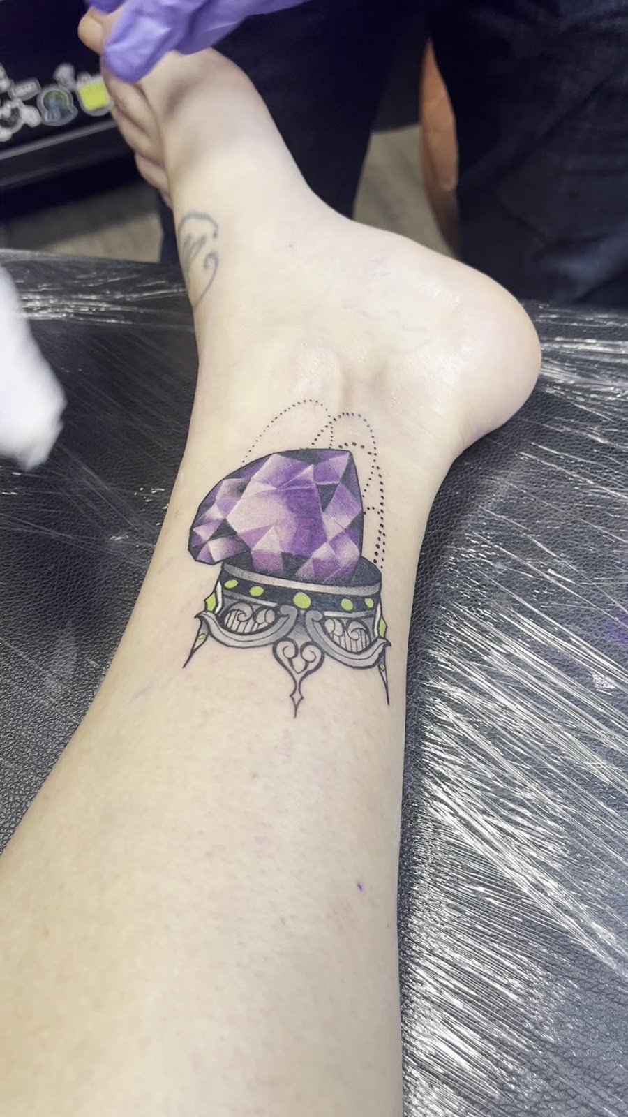 Freshly finished purple faceted gem tattoo with dotwork sparkles on an ankle